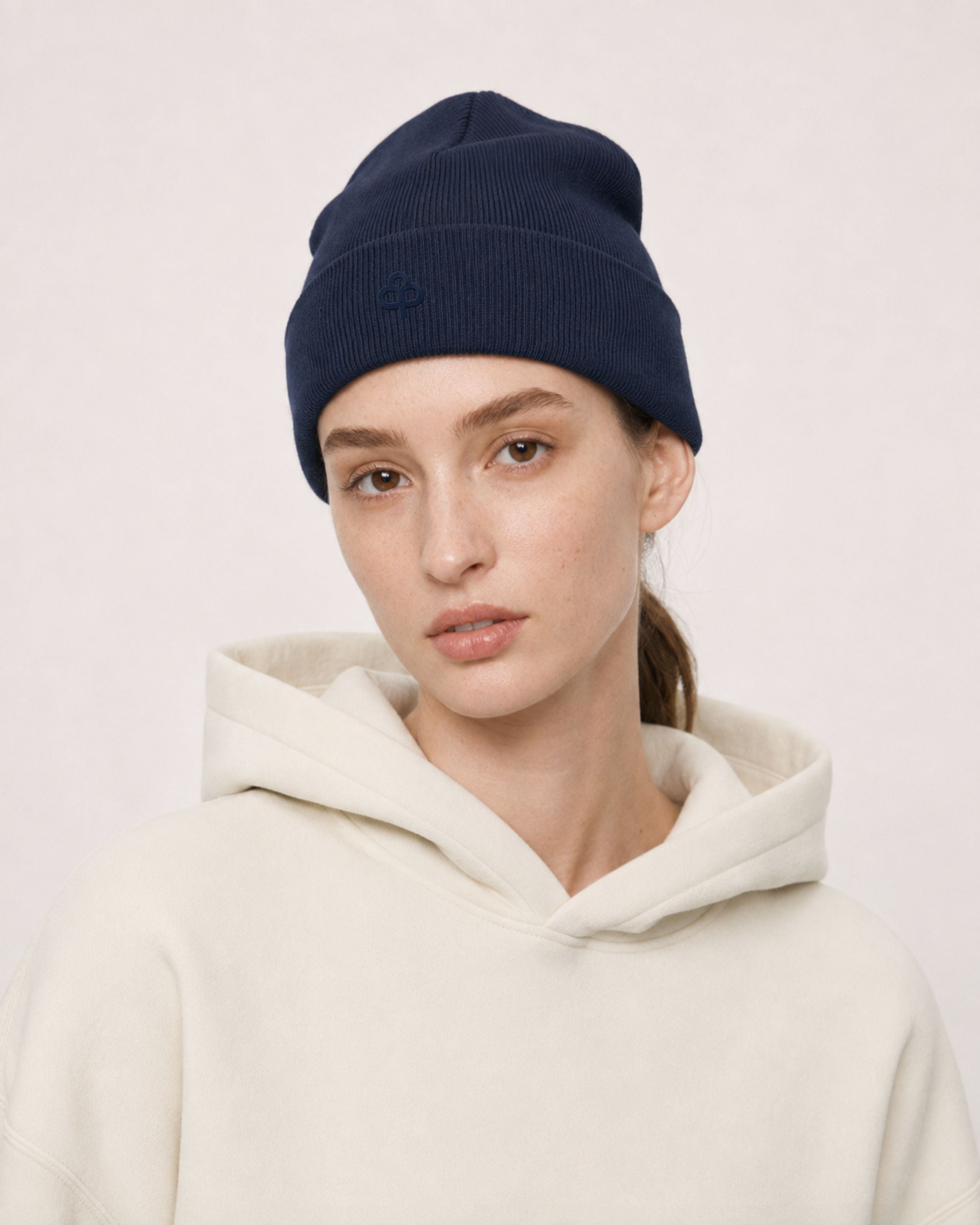 Model in a navy ribbed beanie and cream hoodie, close portrait