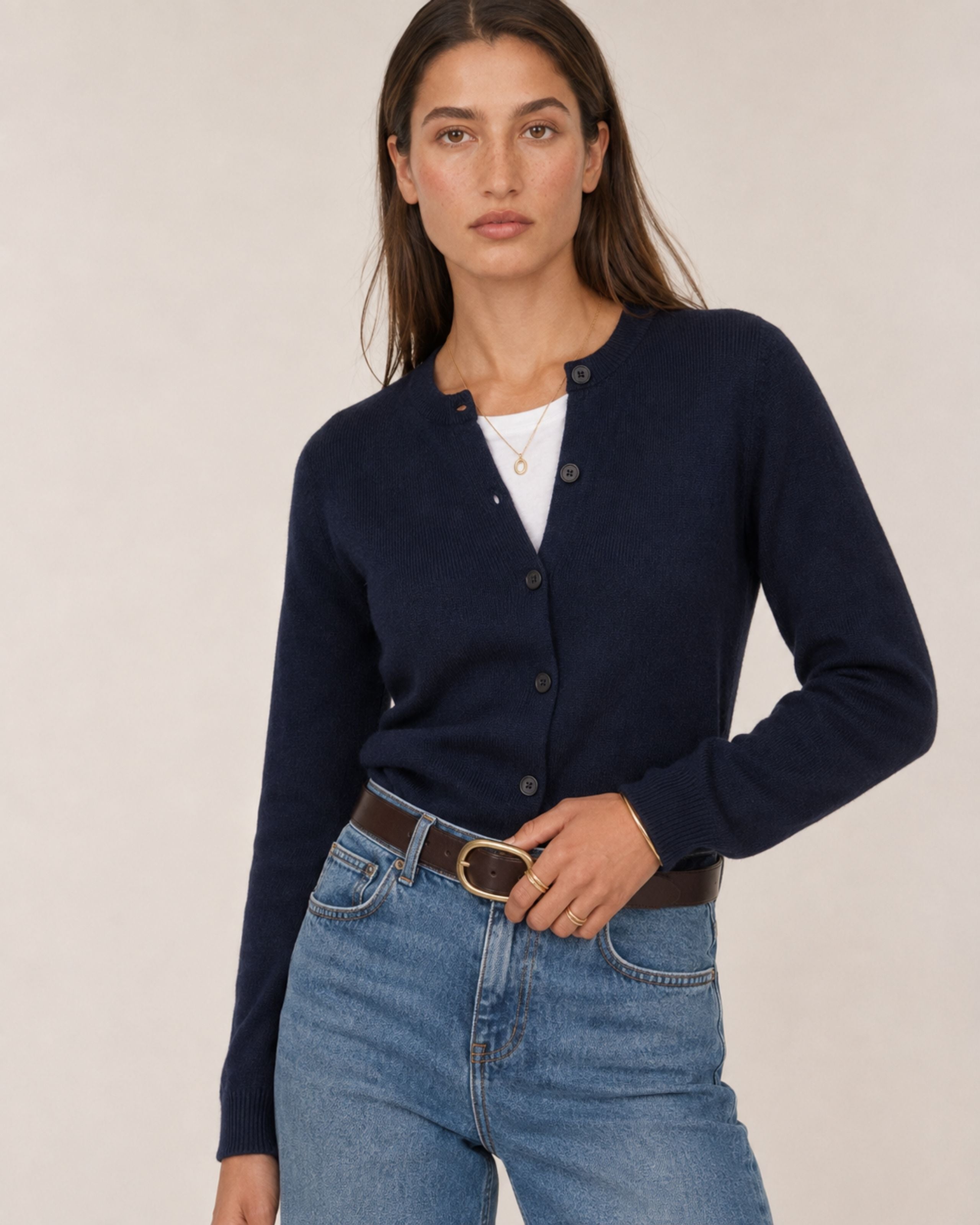 Model in a navy buttoned cardigan and light jeans with a brown belt