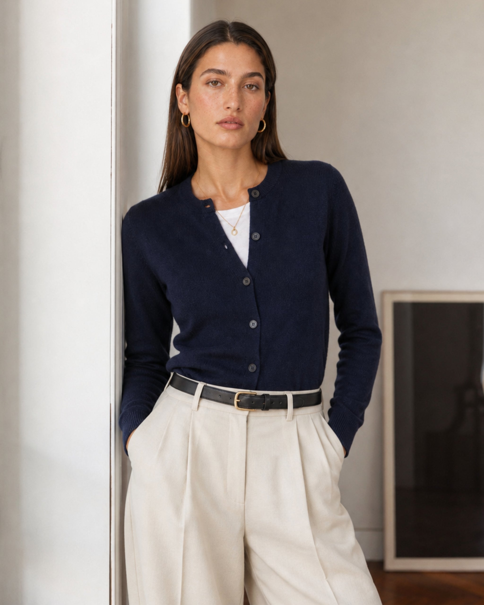 Vrouw in merinocardigan in marineblauw en crème pleated broek binnen