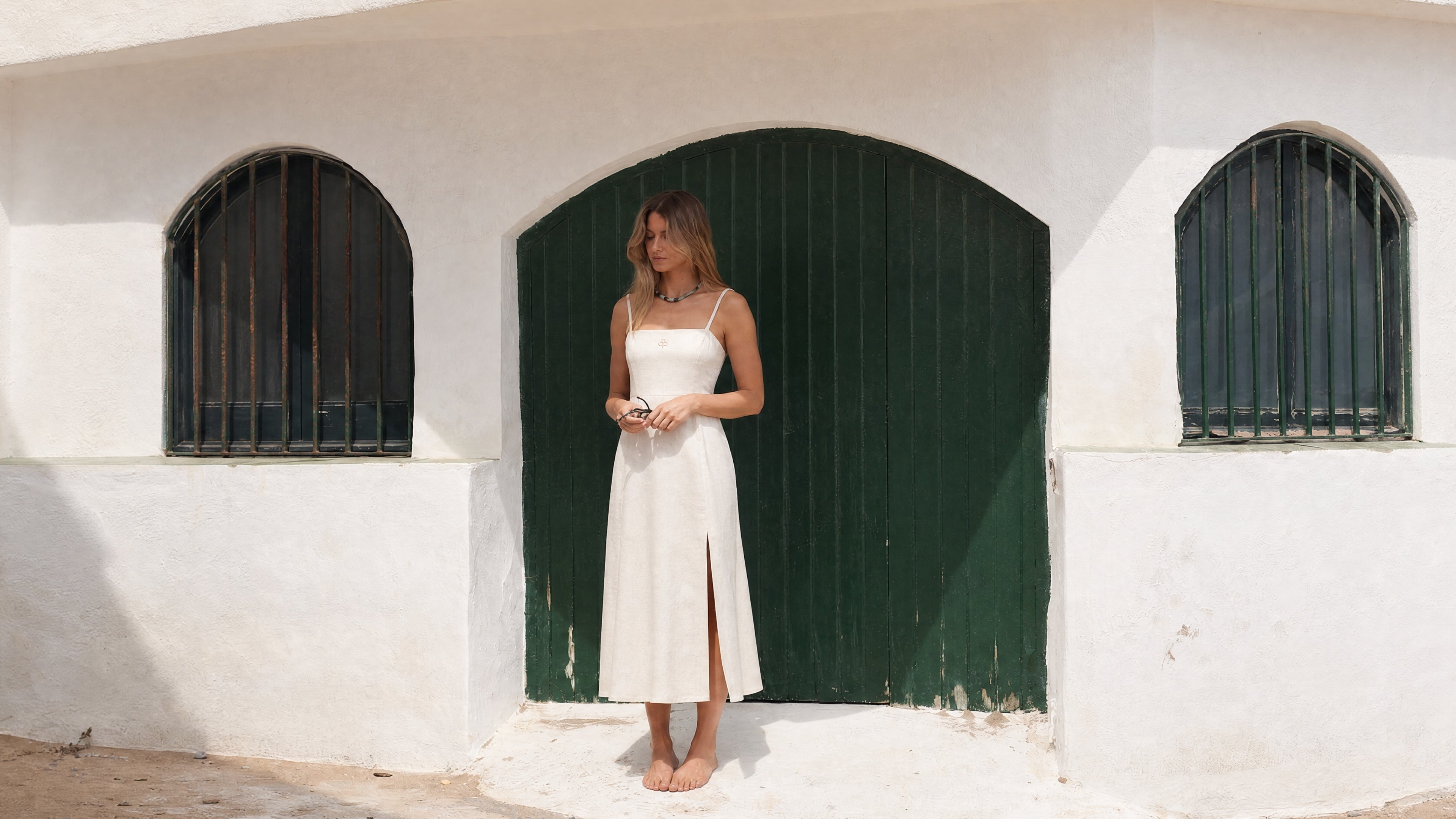 Woman wearing a Pamuuc off white cotton linen midi dress in front of green doors in Garraf.