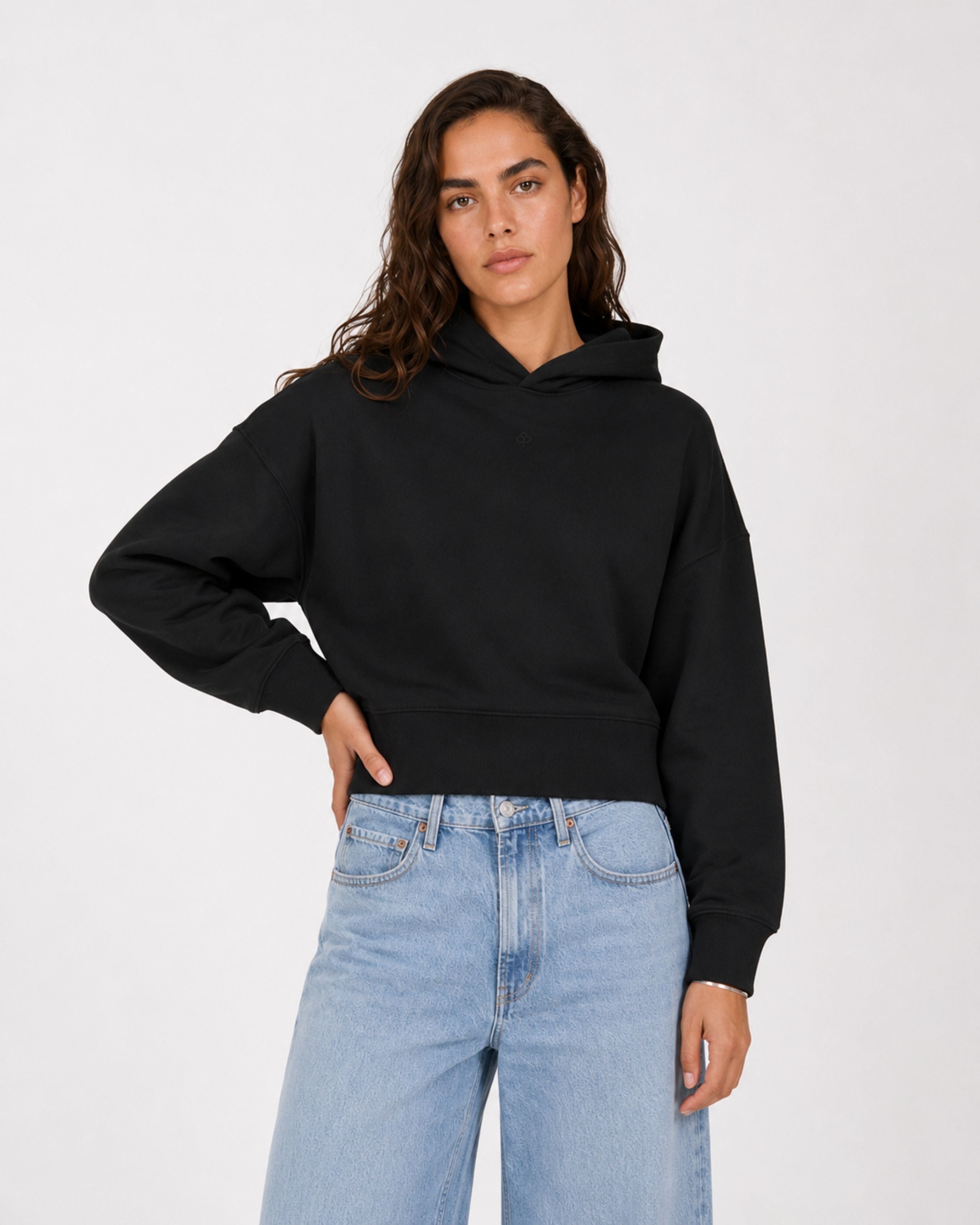 Model in a black hoodie and light jeans, hand on hip