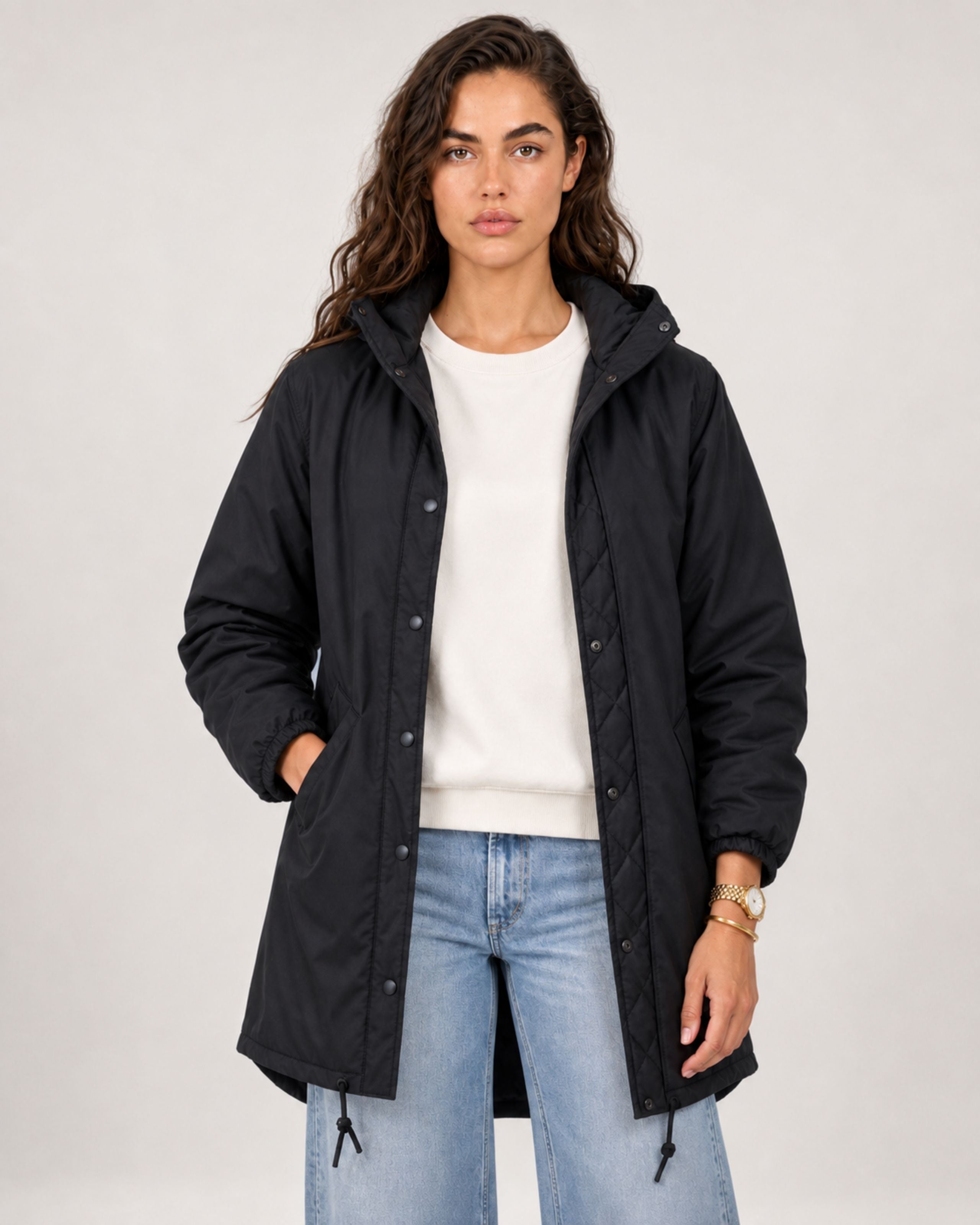Model in an open black parka over a white top and light jeans, front view