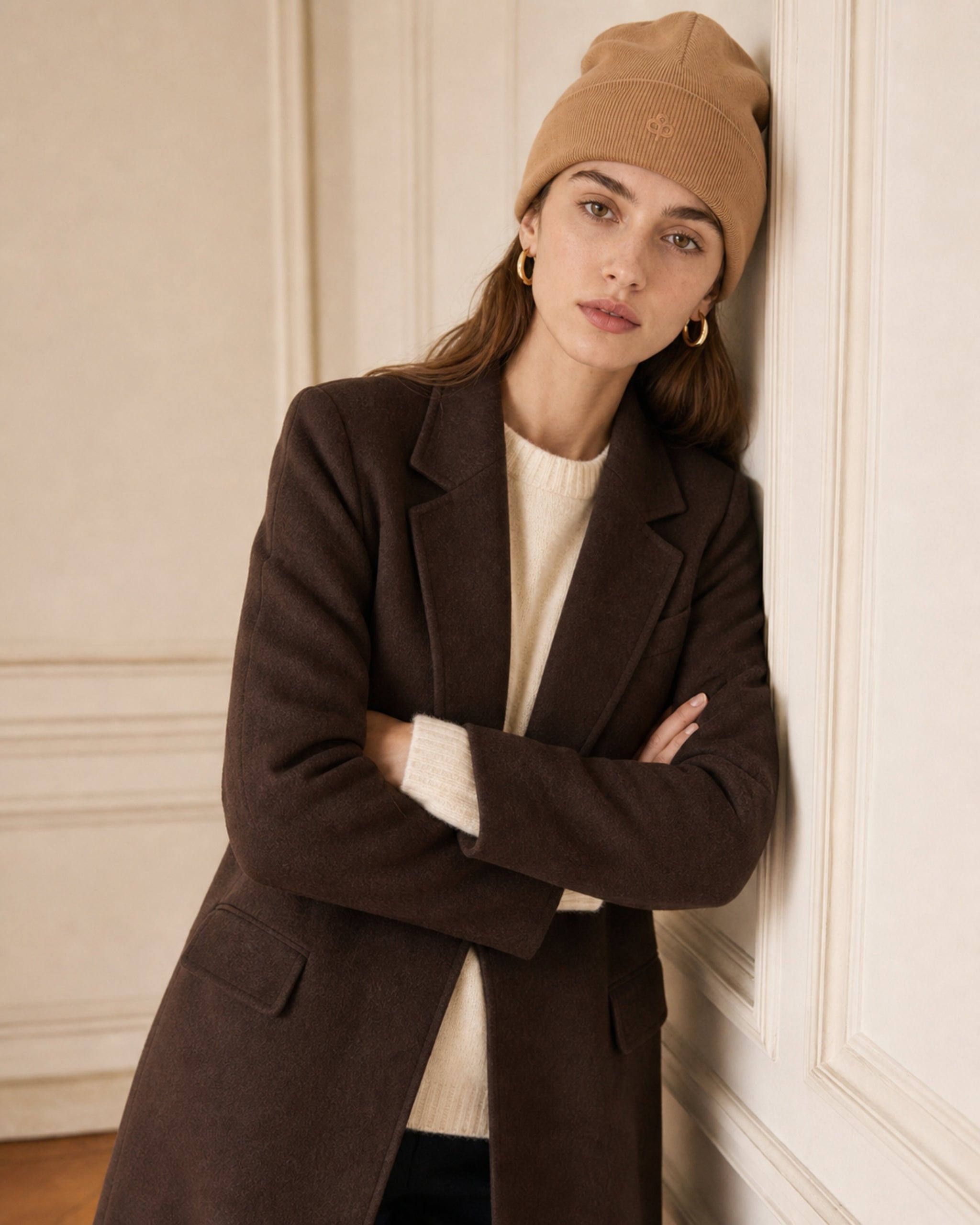 Vrouw in geribde beanie in camel en bruin wollen jas, armen over elkaar