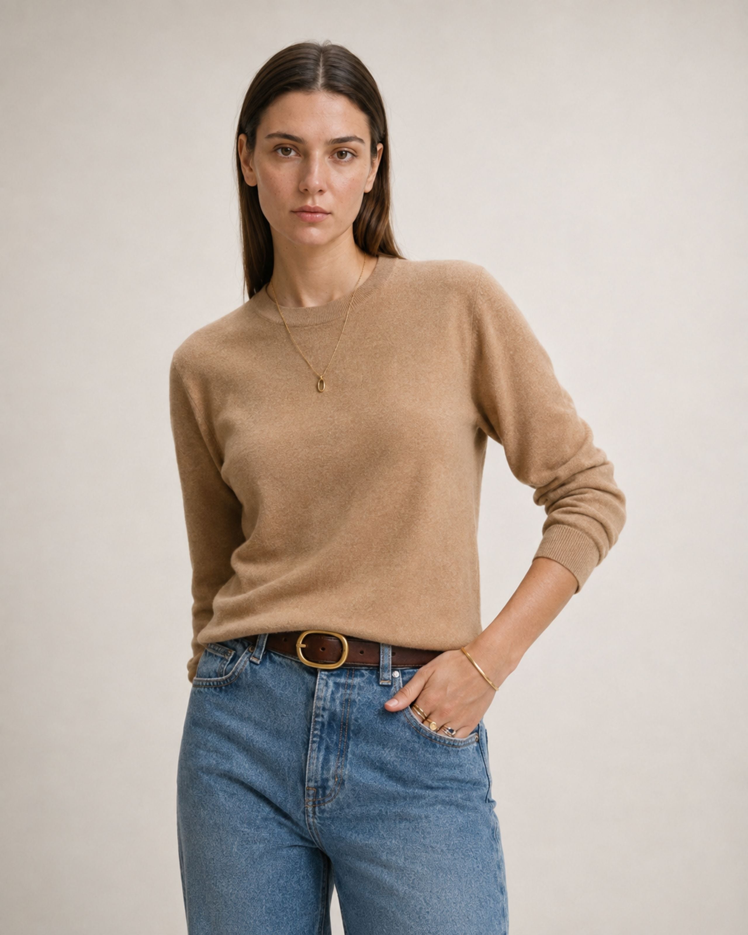 Model in a camel wool sweater tucked into light jeans with a brown belt