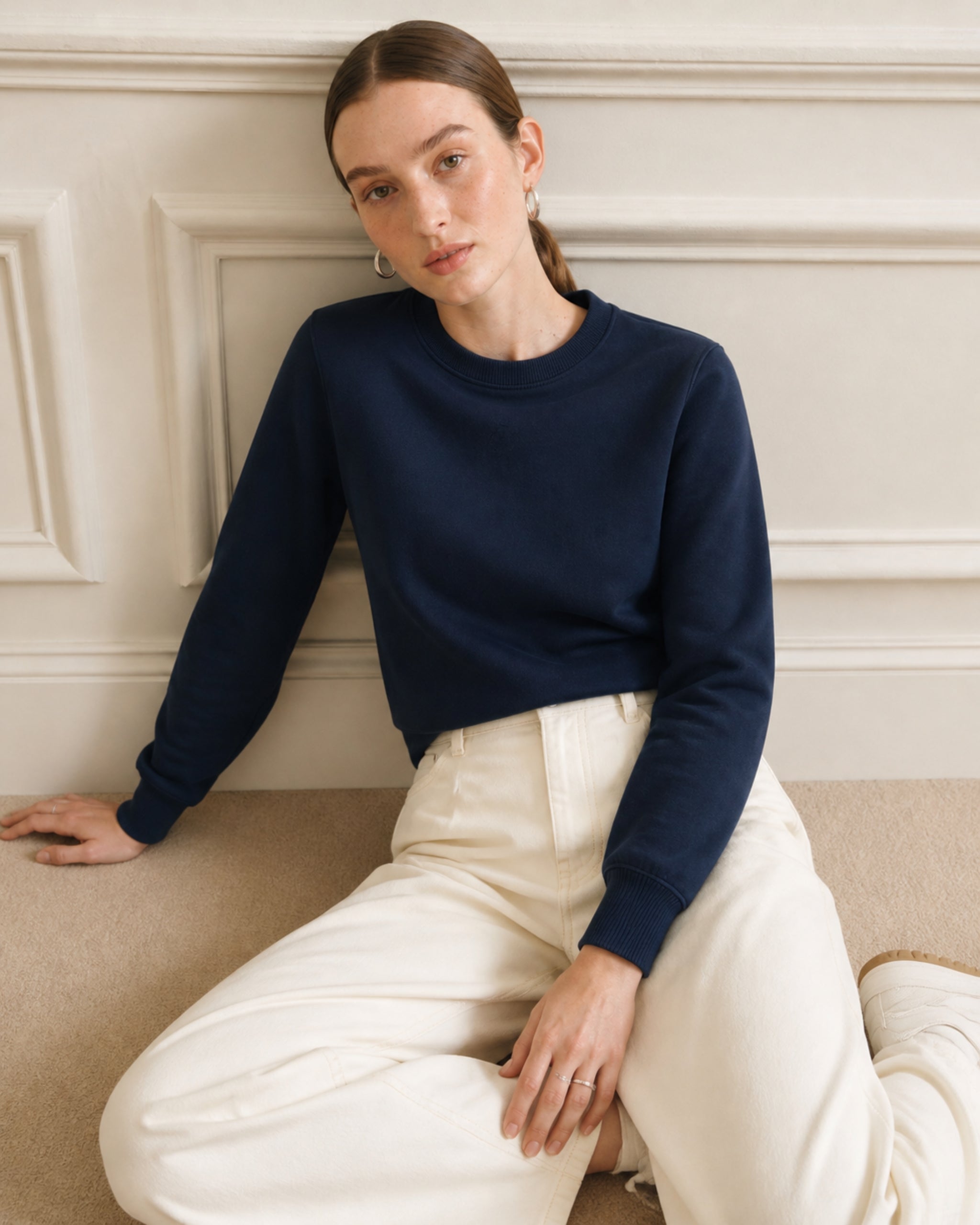 Vrouw in katoenen sweatshirt in marineblauw en broek in crème zittend op een bank