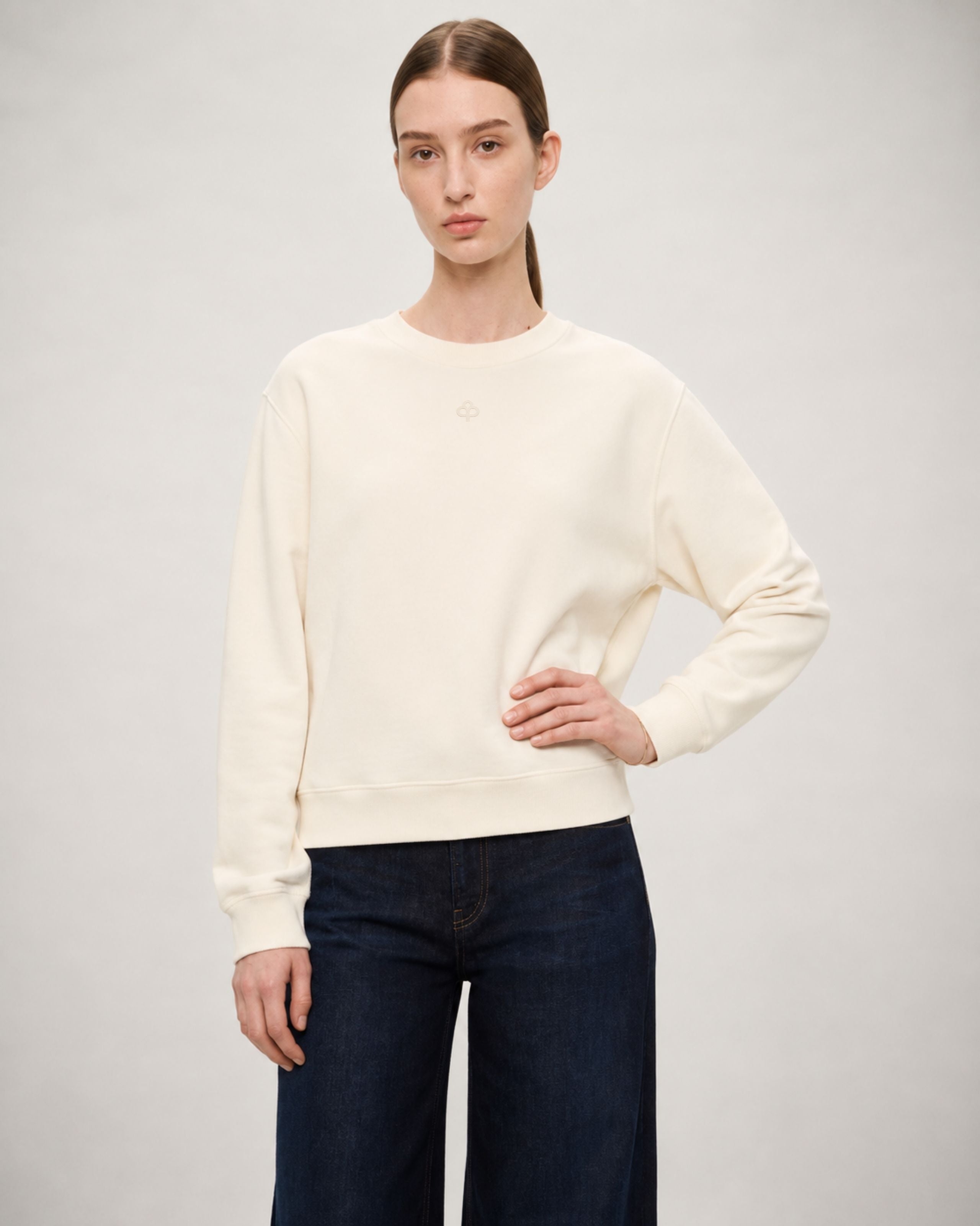 Model in an off-white sweatshirt and dark jeans, hands at her sides